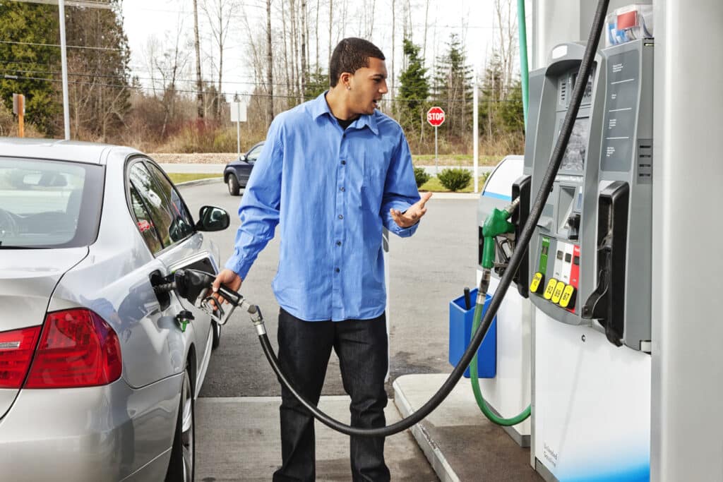 Male in a blue shirt looking confused whilst putting petrol in his car