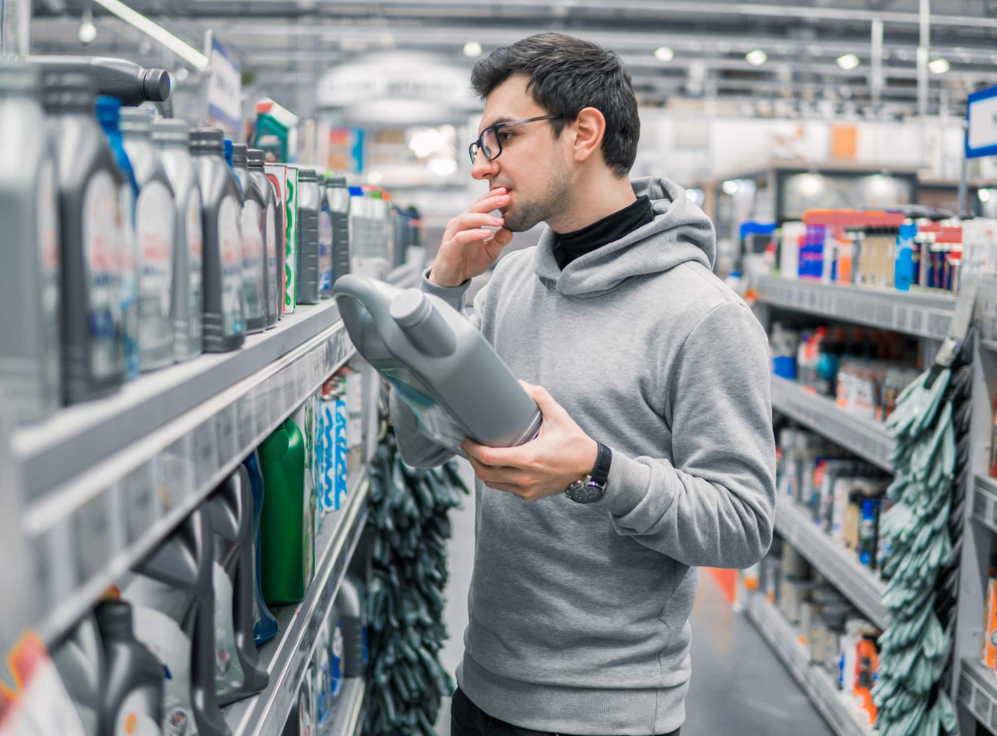 male customer buying engine lubricating oil in the car supermarket. Difficult decision which motor oil to buy